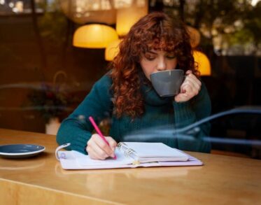 Woman Holds a Hot Cup and Writes in a Cafe