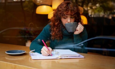 Woman Holds a Hot Cup and Writes in a Cafe